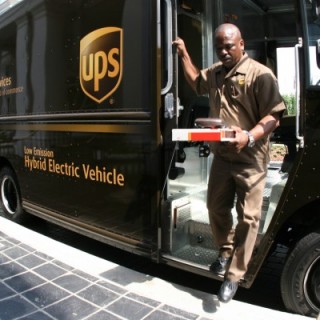 UPS employee in uniform with package, in front of truck with logo
