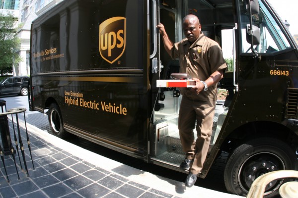 UPS employee in uniform with package, in front of truck with logo