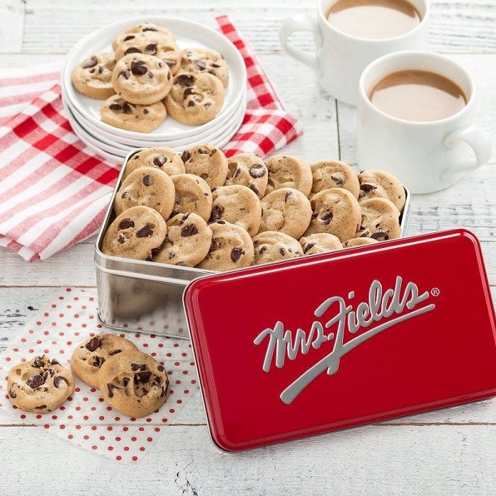 mrs fields cookies in a tin with logo and around it on white plates